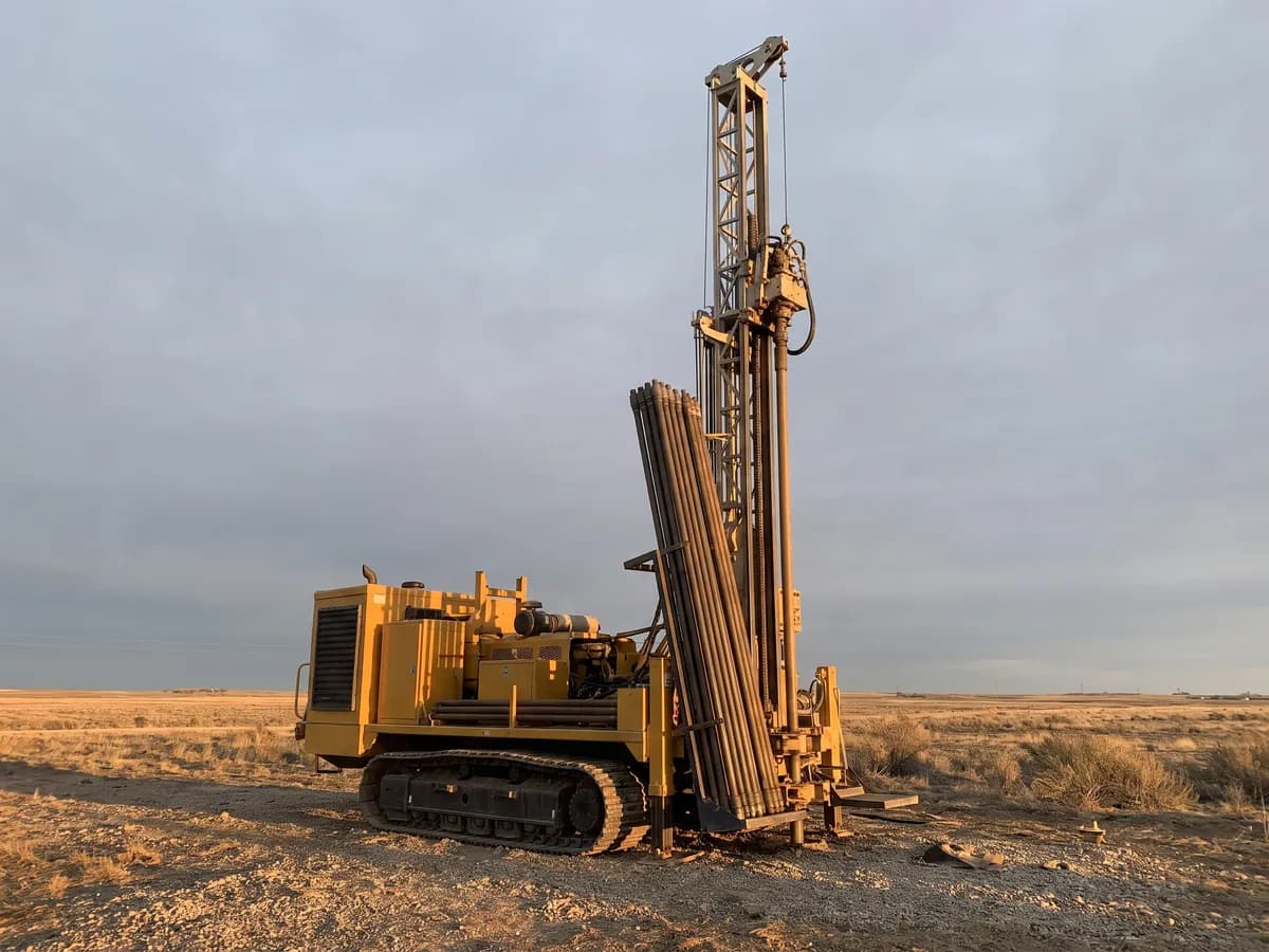 Crawler-mounted water well drilling rig with its mast raised on a drilling site