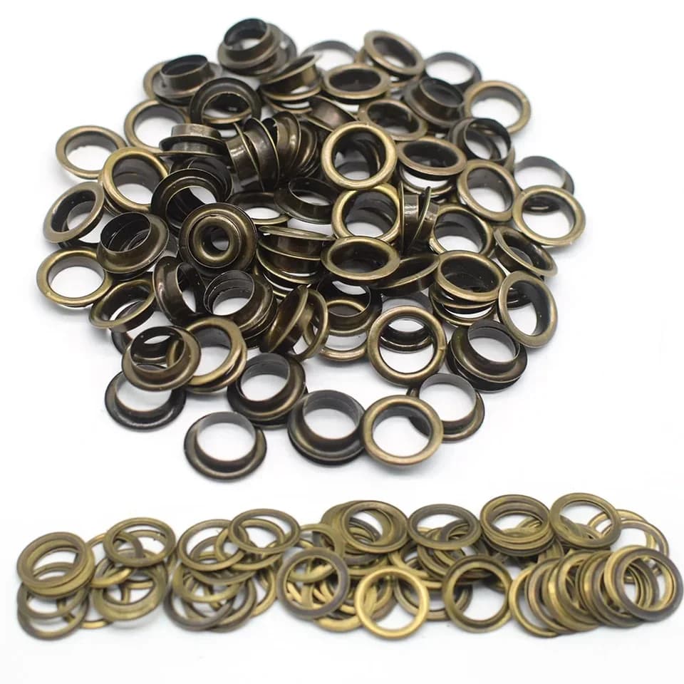 Heavy-Duty Tarpaulin Eyelets: pile of brass-coloured grommets on white.