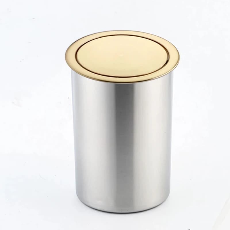 Recessed Countertop Swing Bin: cylindrical container with a gold lid on a plain background.