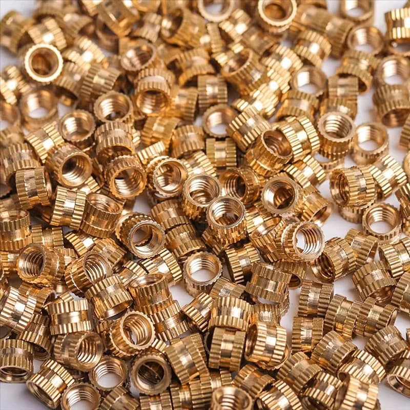 Assortment of brass heat-set insert nuts in various sizes (M2-M6) with knurled exteriors for embedding into 3D printed plastic and resin models.